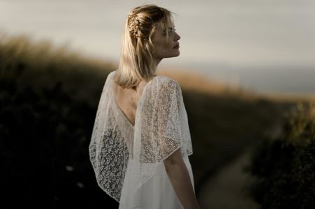 ICY Une robe de mariée bohème chic en dentelle de Calais et crêpe. Volant sur les épaules et quilles légères et transparentes sur les jambes.