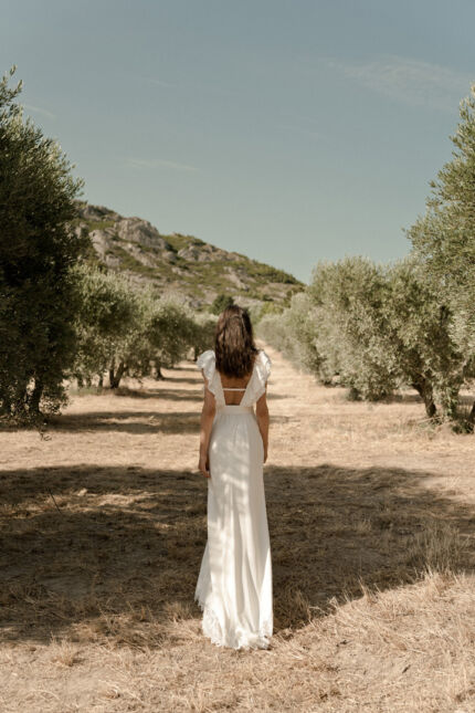 LA ROBE LYRICAL est une robe de mariée moderne en crêpe fluide et guipure écoresponsable. La jupe est fourreau, fendue sur la jambe, la taille marquée par une ceinture et son décolleté carré est orné de grands volants pour une mariée audacieuse. Robe de mariée LYRICAL