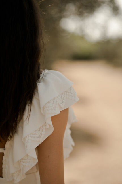 LA ROBE LYRICAL est une robe de mariée moderne en crêpe fluide et guipure écoresponsable. La jupe est fourreau, fendue sur la jambe, la taille marquée par une ceinture et son décolleté carré est orné de grands volants pour une mariée audacieuse. Robe de mariée LYRICAL