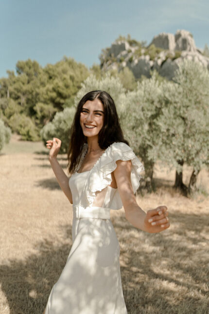 LA ROBE LYRICAL est une robe de mariée moderne en crêpe fluide et guipure écoresponsable. La jupe est fourreau, fendue sur la jambe, la taille marquée par une ceinture et son décolleté carré est orné de grands volants pour une mariée audacieuse. Robe de mariée LYRICAL