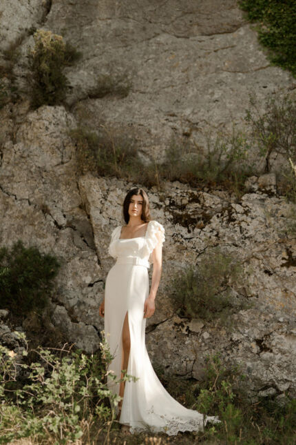 LA ROBE LYRICAL est une robe de mariée moderne en crêpe fluide et guipure écoresponsable. La jupe est fourreau, fendue sur la jambe, la taille marquée par une ceinture et son décolleté carré est orné de grands volants pour une mariée audacieuse. Robe de mariée LYRICAL