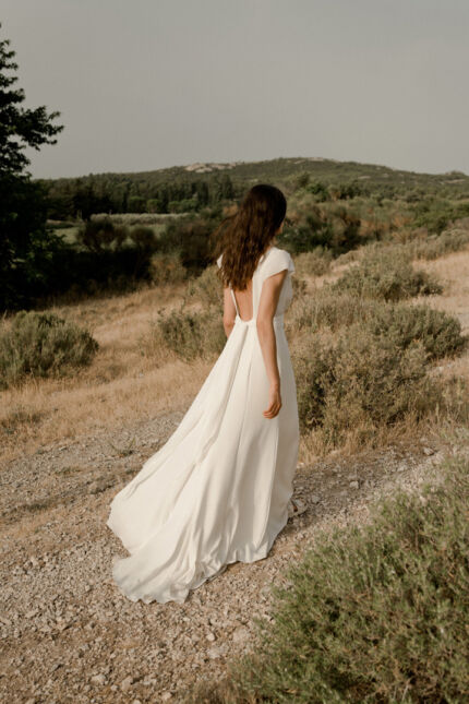 LA ROBE AIGUE MARINE est une robe de mariée moderne et minimaliste en crêpe de soie ultra fluide et légère agrémentée de petites manches volantes et d’une ceinture drapée en mousseline de soie. Elle est sensuelle et légère pour une mariée authentique. LA ROBE AIGUE MARINE