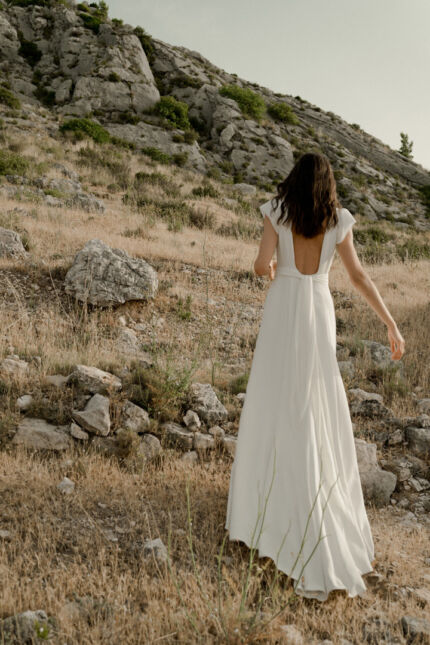 LA ROBE AIGUE MARINE est une robe de mariée moderne et minimaliste en crêpe de soie ultra fluide et légère agrémentée de petites manches volantes et d’une ceinture drapée en mousseline de soie. Elle est sensuelle et légère pour une mariée authentique. LA ROBE AIGUE MARINE