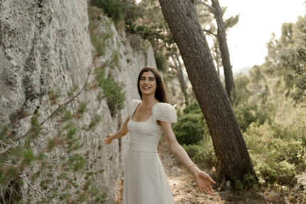 LA ROBE AQUA AURA est une robe de mariée moderne et couture en crêpe de soie. Sa silhouette est longiligne, son buste décolleté carré est habillé de manches courtes gonflantes et sa taille soulignée d’une ceinture finit sur une traine légère en organza, pour une mariée poétique. LA ROBE AQUA AURA