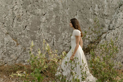 LA ROBE AQUA AURA est une robe de mariée moderne et couture en crêpe de soie. Sa silhouette est longiligne, son buste décolleté carré est habillé de manches courtes gonflantes et sa taille soulignée d’une ceinture finit sur une traine légère en organza, pour une mariée poétique. LA ROBE AQUA AURA