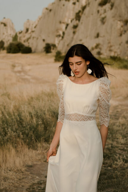 LA ROBE LOOKER est une robe de mariée moderne très chic. En crêpe fluide et guipure écoresponsable, ses manches rehaussées, sa taille transparente et son grand décolleté dans le dos apportent force et originalité pour une mariée affirmée. Bijoux LA ROBE LOOKER