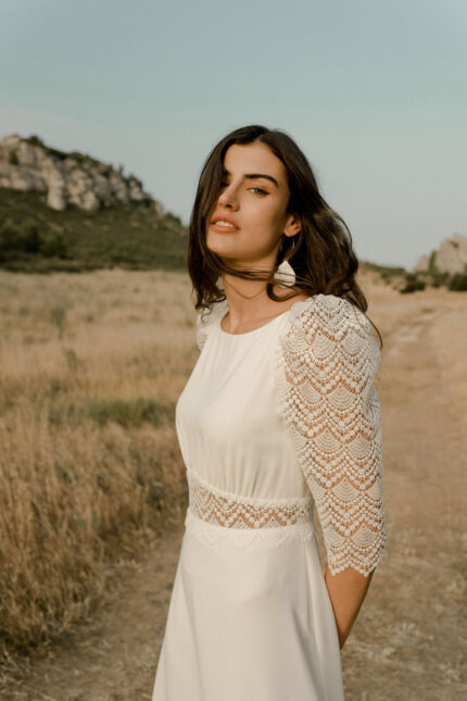 LA ROBE LOOKER est une robe de mariée moderne très chic. En crêpe fluide et guipure écoresponsable, ses manches rehaussées, sa taille transparente et son grand décolleté dans le dos apportent force et originalité pour une mariée affirmée. Bijoux LA ROBE LOOKER