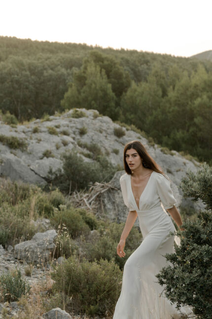 LA ROBE AMBRE est une robe de mariée moderne chic et couture toute en crêpe de soie. Des manches gonflantes à plis dessinent les épaules, son grand décolleté sensuel et sa fente conviendront à une mariée amazone des temps modernes. LA ROBE AMBRE