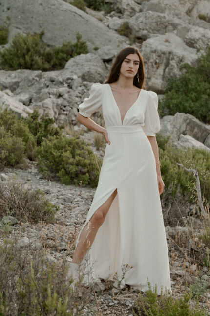 LA ROBE AMBRE est une robe de mariée moderne chic et couture toute en crêpe de soie. Des manches gonflantes à plis dessinent les épaules, son grand décolleté sensuel et sa fente conviendront à une mariée amazone des temps modernes. LA ROBE AMBRE