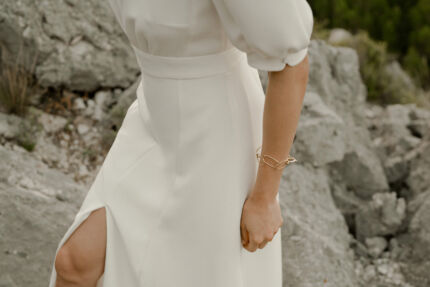 LA ROBE AMBRE est une robe de mariée moderne chic et couture toute en crêpe de soie. Des manches gonflantes à plis dessinent les épaules, son grand décolleté sensuel et sa fente conviendront à une mariée amazone des temps modernes. LA ROBE AMBRE