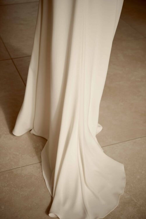 NIMIO est une robe de mariée moderne et chic, en crêpe de soie ornée d'une ceinture et de petites manches drapées.