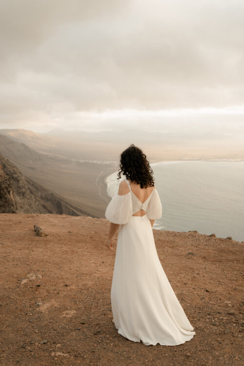 PODER PARA TI est un ensemble de mariée moderne et sexy, composé d'un bustier de mariée drapé de mousseline de soie plissée et d'une jupe de mariée fluide en crêpe de soie. Les manches bouffantes de cet ensemble de mariage sont amovibles.