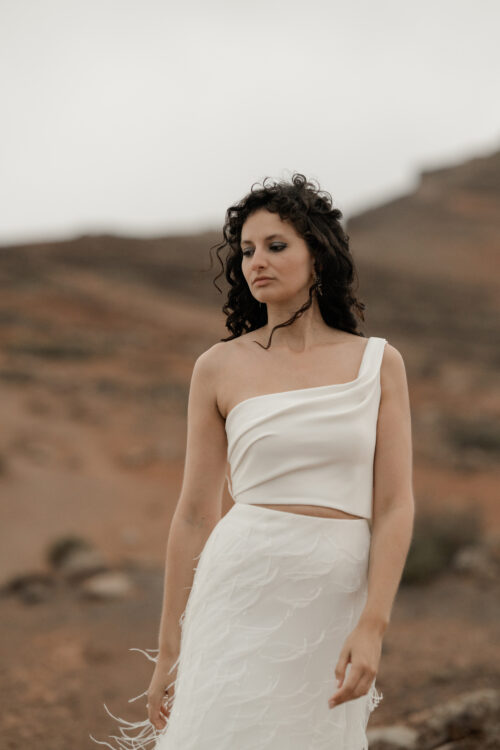 ORIGINAL est un ensemble de mariée audacieux pour une tenue de mariée moderne. Il est composé d'un bustier de mariage asymétrique drapé de crêpe de soie et d'une jupe de mariée en broderie de plumes. La jupe de mariée, fendue sur le côté, en fait une tenue de mariée sexy. L'audace de cette tenue de mariée sera parfaite pour un mariage chic et rock.