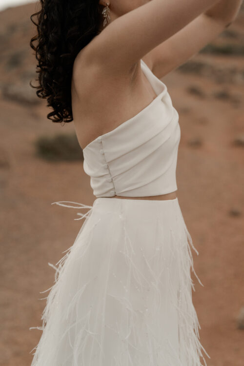 ORIGINAL est un ensemble de mariée audacieux pour une tenue de mariée moderne. Il est composé d'un bustier de mariage asymétrique drapé de crêpe de soie et d'une jupe de mariée en broderie de plumes. La jupe de mariée, fendue sur le côté, en fait une tenue de mariée sexy. L'audace de cette tenue de mariée sera parfaite pour un mariage chic et rock.