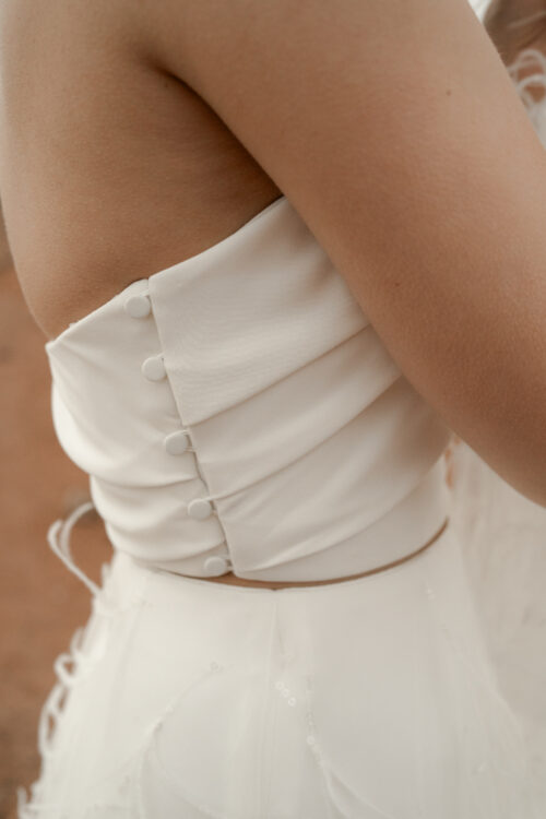 ORIGINAL est un ensemble de mariée audacieux pour une tenue de mariée moderne. Il est composé d'un bustier de mariage asymétrique drapé de crêpe de soie et d'une jupe de mariée en broderie de plumes. La jupe de mariée, fendue sur le côté, en fait une tenue de mariée sexy. L'audace de cette tenue de mariée sera parfaite pour un mariage chic et rock.