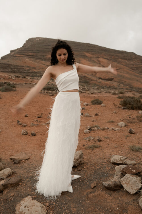 ORIGINAL est un ensemble de mariée audacieux pour une tenue de mariée moderne. Il est composé d'un bustier de mariage asymétrique drapé de crêpe de soie et d'une jupe de mariée en broderie de plumes. La jupe de mariée, fendue sur le côté, en fait une tenue de mariée sexy. L'audace de cette tenue de mariée sera parfaite pour un mariage chic et rock.