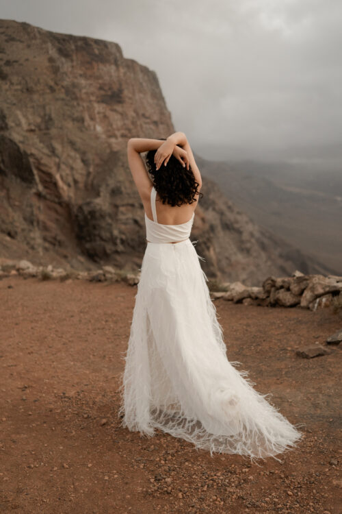 ORIGINAL est un ensemble de mariée audacieux pour une tenue de mariée moderne. Il est composé d'un bustier de mariage asymétrique drapé de crêpe de soie et d'une jupe de mariée en broderie de plumes. La jupe de mariée, fendue sur le côté, en fait une tenue de mariée sexy. L'audace de cette tenue de mariée sera parfaite pour un mariage chic et rock.