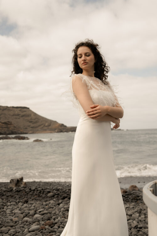 Passion est une robe de mariée minimaliste en crêpe eco-friendly avec de fines bretelles et une fente sur le côté. Son dos-nu original en fait une robe de mariée moderne. Cette robe de mariée simple pourra être portée avec PROSPER notre petit top de mariage transparent en broderie de perles ou en broderie de plumes. Bijoux @anthemis.paris