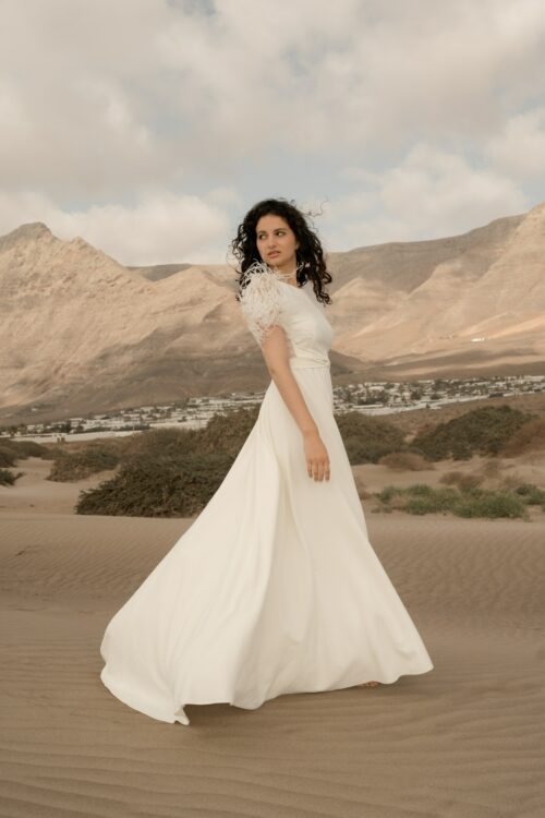 PROMISE est une robe de mariée moderne en crêpe eco-friendly avec des manches courtes en broderie de plumes. C’est une robe de mariée chic avec une jupe de mariée ample et fendue. Cette robe de mariée dos nu sera parfaite pour un mariage cool et chic. En réalisant votre robe de mariée sur mesure, vous pourrez opter pour les manches de votre choix. Bijoux @anthemis.paris