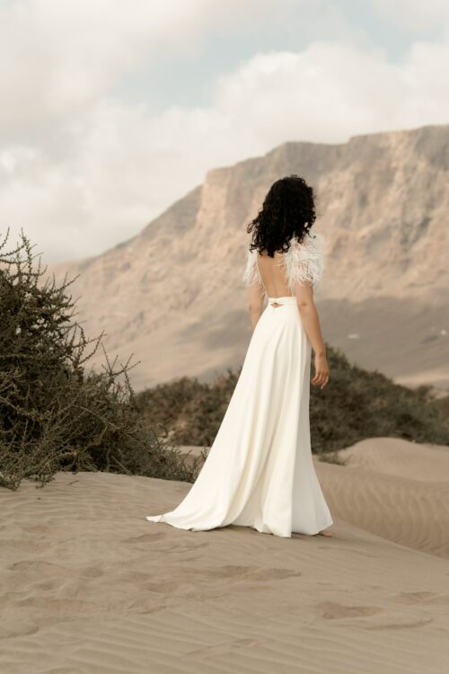 PROMISE est une robe de mariée moderne en crêpe eco-friendly avec des manches courtes en broderie de plumes. C’est une robe de mariée chic avec une jupe de mariée ample et fendue. Cette robe de mariée dos nu sera parfaite pour un mariage cool et chic. En réalisant votre robe de mariée sur mesure, vous pourrez opter pour les manches de votre choix. Bijoux @anthemis.paris