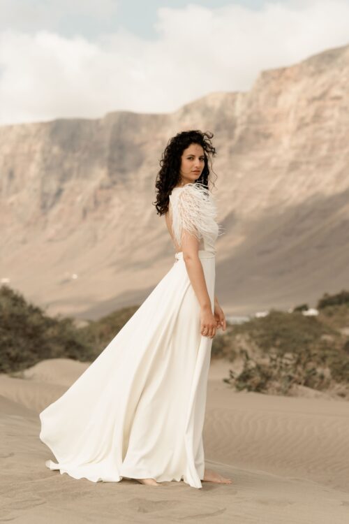 PROMISE est une robe de mariée moderne en crêpe eco-friendly avec des manches courtes en broderie de plumes. C’est une robe de mariée chic avec une jupe de mariée ample et fendue. Cette robe de mariée dos nu sera parfaite pour un mariage cool et chic. En réalisant votre robe de mariée sur mesure, vous pourrez opter pour les manches de votre choix. Bijoux @anthemis.paris