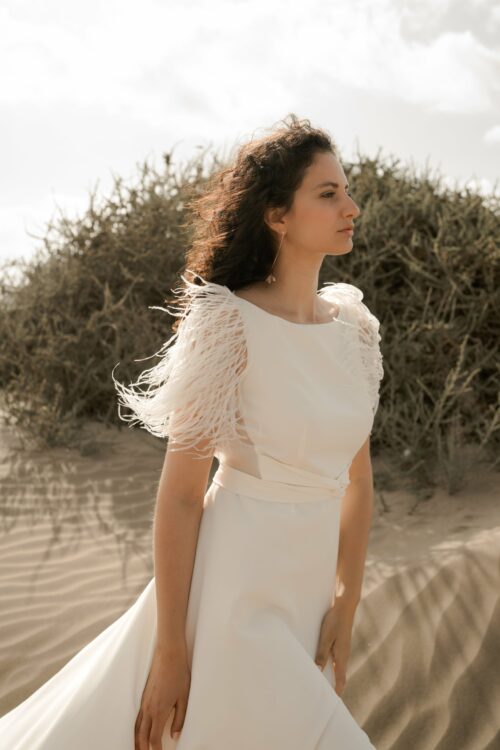 PROMISE est une robe de mariée moderne en crêpe eco-friendly avec des manches courtes en broderie de plumes. C’est une robe de mariée chic avec une jupe de mariée ample et fendue. Cette robe de mariée dos nu sera parfaite pour un mariage cool et chic. En réalisant votre robe de mariée sur mesure, vous pourrez opter pour les manches de votre choix. Bijoux @anthemis.paris