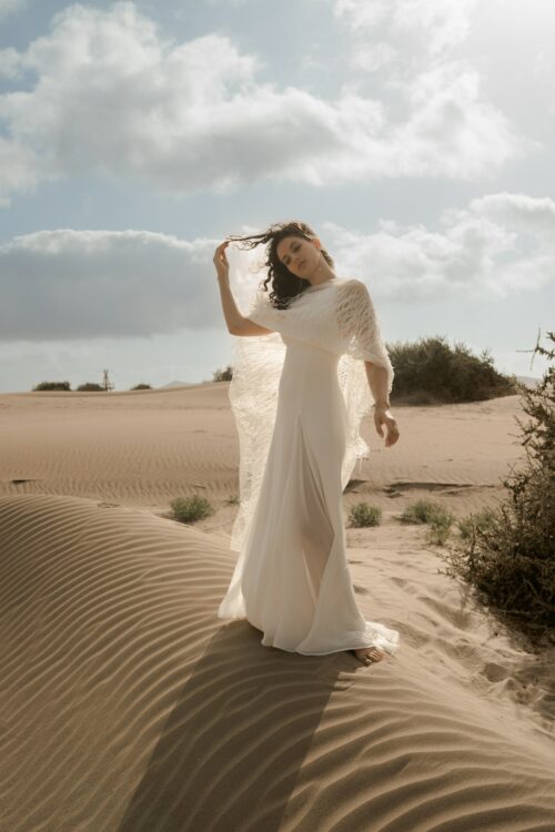 PARADISE est une robe de mariée chic en crêpe de soie. Son décolleté « emmanchures américaines » et son dos habillé de bretelles en font une robe de mariée minimaliste élégante. La jupe est incrustée de mousseline de soie pour faire une robe de mariée fluide. Bijoux @anthemis.paris . « Plumes » est une étole de mariée en broderie de plumes.