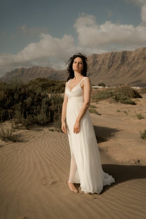 PRECIOSO est une robe de mariée empire toute en mousseline de soie. Son buste est drapé de mousseline de soie plissée. Sa jupe de mariée en mousseline de soie voluptueuse est fendue au milieu devant. C’est une robe de mariée légère pour un mariage romantique et moderne. Bijoux @anthemis.paris