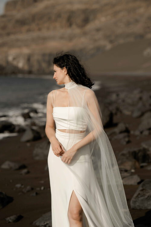 PUREMENT et SIMPLEMENT est un ensemble de mariée moderne. C’est une tenue de mariée minimaliste composée d’un bustier drapé légèrement de crêpe de soie et d’une jupe de mariée fluide fendue en crêpe de soie. Pour une tenue de cérémonie laïque, vous pourrez choisir de porter notre voile-étole de mariée Paco brodé de motifs floraux.