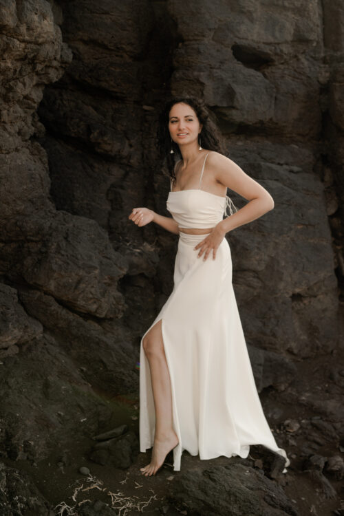 PUREMENT et SIMPLEMENT est un ensemble de mariée moderne. C’est une tenue de mariée minimaliste composée d’un bustier drapé légèrement de crêpe de soie et d’une jupe de mariée fluide fendue en crêpe de soie.