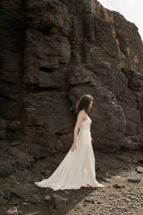 PUREMENT et SIMPLEMENT est un ensemble de mariée moderne. C’est une tenue de mariée minimaliste composée d’un bustier drapé légèrement de crêpe de soie et d’une jupe de mariée fluide fendue en crêpe de soie.