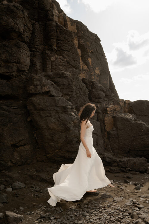 PUREMENT et SIMPLEMENT est un ensemble de mariée moderne. C’est une tenue de mariée minimaliste composée d’un bustier drapé légèrement de crêpe de soie et d’une jupe de mariée fluide fendue en crêpe de soie.